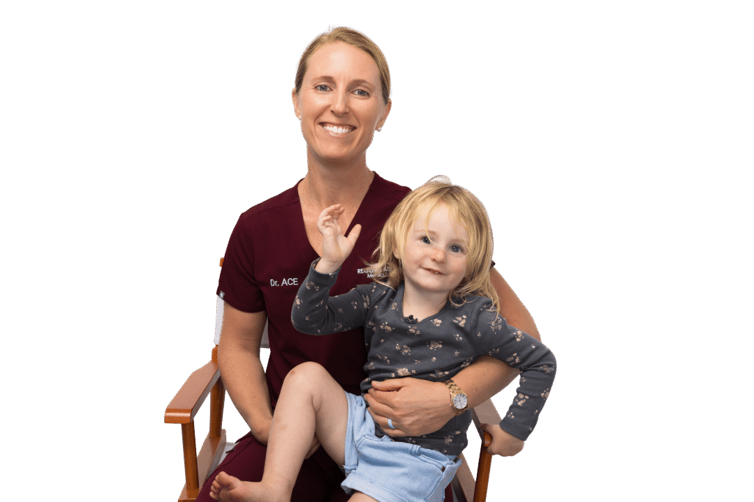 Medical provider holding a small child while both smile in a seated family portrait.