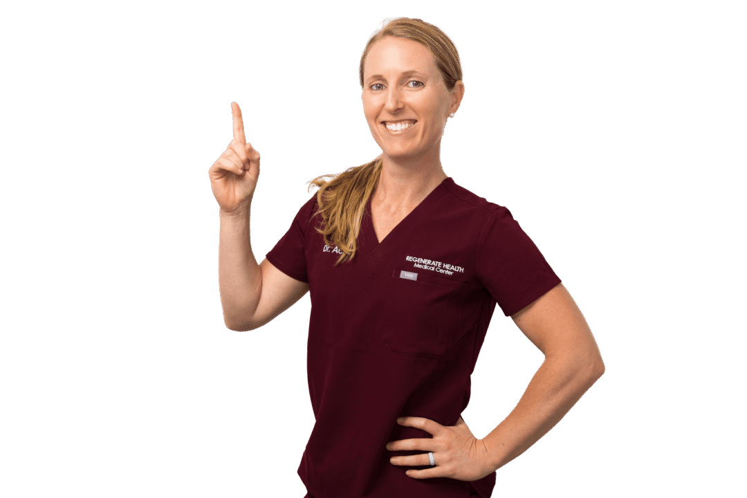 Female medical provider in burgundy scrubs smiling and posing with one hand on hip.