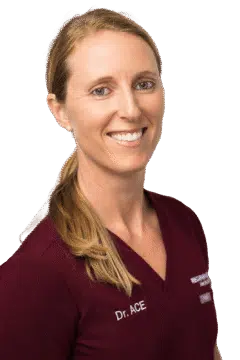 Female medical provider in burgundy scrubs smiling in a vertical professional portrait