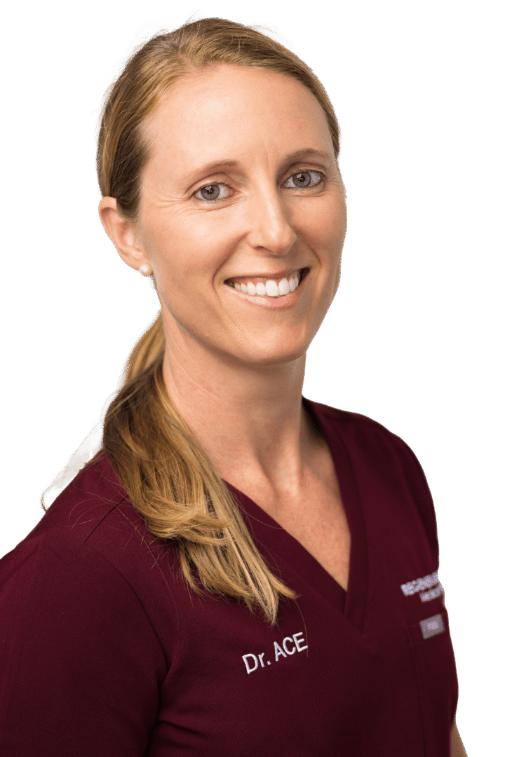 Female medical provider in burgundy scrubs smiling in a vertical professional portrait
