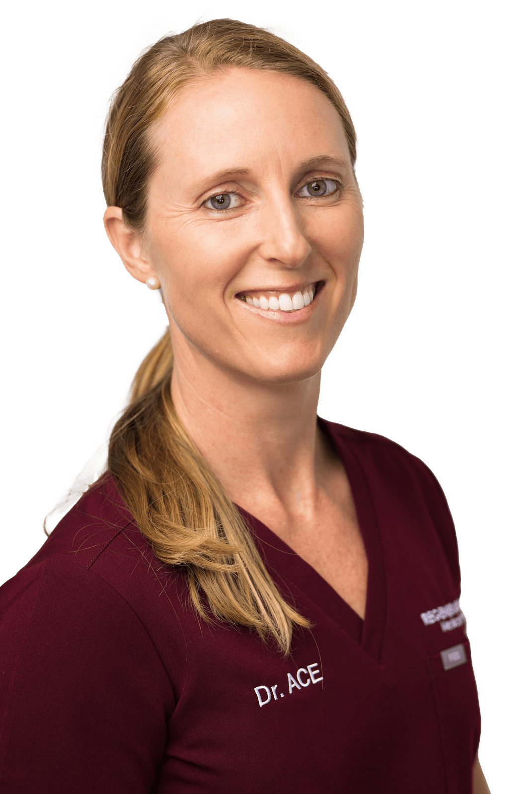 Female medical provider in burgundy scrubs smiling in a vertical professional portrait