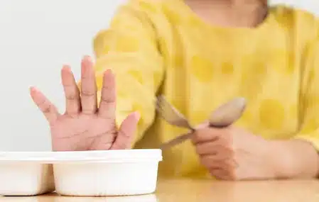 Person pushing away a food container, representing appetite suppression